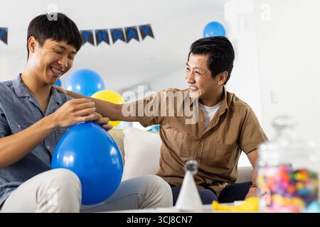 Vater und Sohn feiern zu Hause Geburtstag, lächeln und halten Ballons Stockfoto