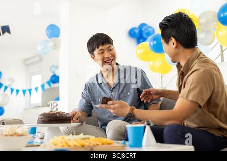 Wir feiern Geburtstag, zwei Freunde genießen Kuchen und Lachen auf der Heimfeier Stockfoto