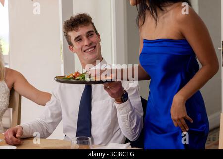 Lächelnder Mann in weißem Hemd, der bei der Hochzeit einen Teller von einer Frau in blauem Kleid empfängt Stockfoto