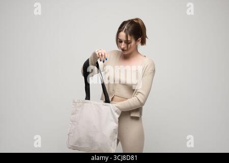 Frau in beigefarbenem Outfit, die umweltfreundliche Stofftragetasche hält Stockfoto
