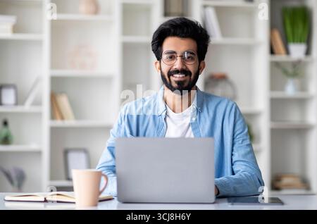 Attraktiver Junger Indischer Mann Sitzt Am Schreibtisch Mit Laptop Zu Hause Stockfoto