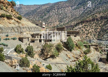Traditionelles Steindorf im marokkanischen Atlasgebirge, umgeben von felsigen Hängen und verstreuten grünen Bäumen, die sich in die trockene Wüstenlandschaft einfügen Stockfoto