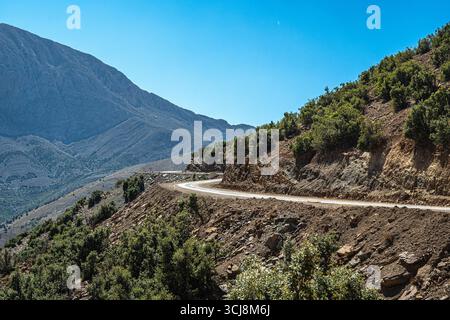 Atlas Mountains Marokko trockene Hügel mit verstreuten trockenen Bäumen und felsigen Hängen unter hellblauem Himmel in abgelegener Wüstenlandschaft Stockfoto