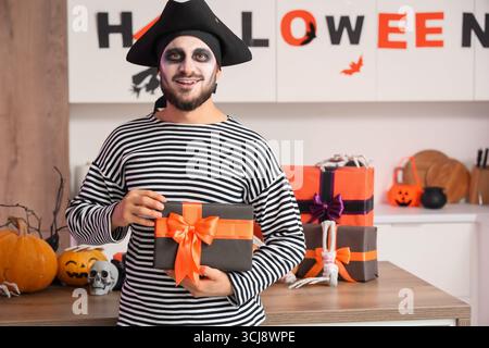 Junger glücklicher Mann, verkleidet als Pirate zu Halloween mit Geschenkbox in dekorierter Küche Stockfoto