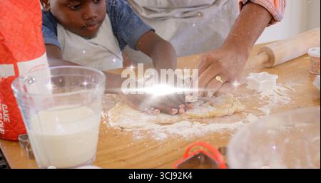 Vater und Sohn in Schürzen kneten Teig auf Küchenarbeitsplatte, mit Nudelnadel und Streuseln Stockfoto
