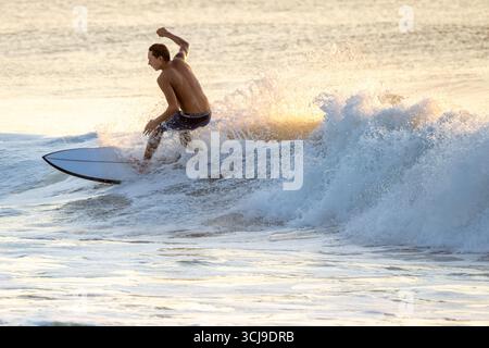 Junger Mann beim Surfen bei Sonnenaufgang auf Amelia Island in der Nähe von Amelia am Sea Pier in Fernandina Beach, Florida. (USA) Stockfoto