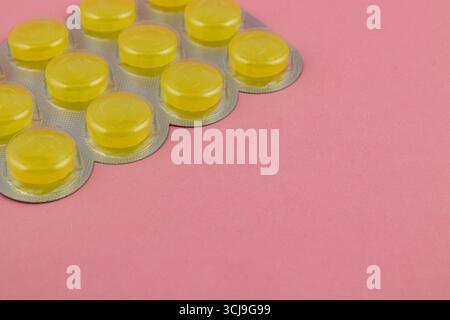 Eine Packung mit hellgelben Tabletten befindet sich ordentlich auf einer weichen rosa Oberfläche. Die runden Tabletten sind glänzend und reflektieren das Licht, was für eine auffällige CO sorgt Stockfoto