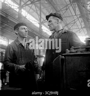 Zwei Arbeitergenossen diskutieren eine Aufgabe an einer Drehmaschine in einer Fabrikwerkstatt in Sloviansk, 1970er Jahre Das Archivfoto vermittelt eine warme Atmosphäre der Freundschaft und Mentorität in einem sowjetischen Werkkollektiv. Diese Szene friedlicher, kreativer Arbeit und menschlicher Beziehungen ist ein Symbol für das Leben im Donbass vor dem Krieg Stockfoto