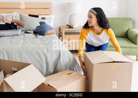 Junge Frau, die Pappkartons im Schlafzimmer packt und sich auf den Umzug vorbereitet Stockfoto
