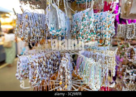 Farbenfrohe handgefertigte Muschelarmbänder auf dem Straßenmarkt. Ausstellung von lebendigen handgefertigten Armbändern mit Muscheln und Perlen, die auf einem Regal auf einem Straßenmarkt im Freien hängen Stockfoto