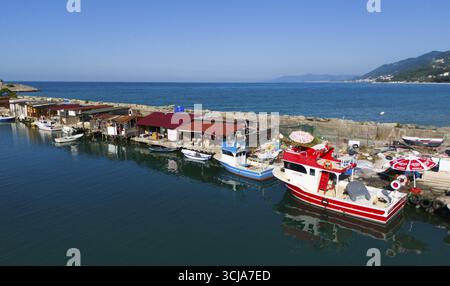 Fischerhafen mit farbenfrohen Booten und Hütten entlang einer ruhigen Küste unter klarem Himmel, Luftsicht, Ginolu, Provinz Kastamonu, Türkei Stockfoto