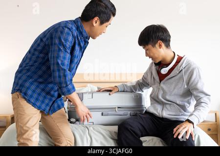 Koffer packen, zwei asiatische Männer bereiten sich auf die Reise zu Hause vor Stockfoto