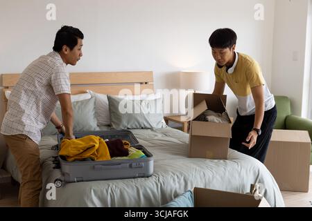 Koffer und Kisten packen, zwei Männer organisieren Sachen im Schlafzimmer Stockfoto