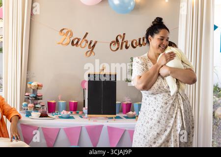Lächelnde Frau, die das Baby bei der Babyparty mit Dekorationen und Cupcakes hält Stockfoto