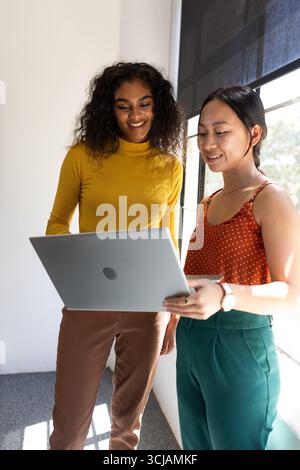 Zwei Frauen, die im Büro an einem Laptop arbeiten, Ideen austauschen und lächeln Stockfoto