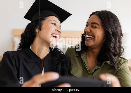 Abschlussfeier, Mutter und Tochter lachen und machen zu Hause Selfie Stockfoto