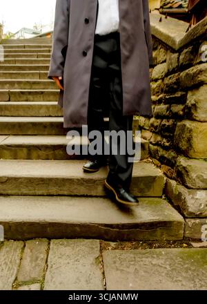 Eine Person in einem grauen Mantel und einer schwarzen Hose läuft eine Steintreppe hinunter. Stockfoto
