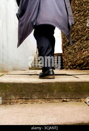 Eine Person in dunklem Mantel und Hose geht eine Treppe hinauf. Stockfoto