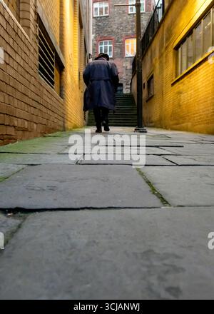 Eine Person mit Hut und Mantel geht eine Treppe hinauf in einer engen Gasse. Stockfoto