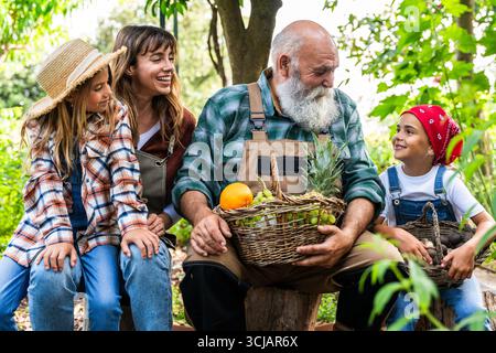 Eine fröhliche Familie, darunter ein Großvater, eine Mutter und zwei Töchter, macht eine Pause von der Arbeit auf einer Bio-Farm, während sie stolz Freshlenkörbe zeigt Stockfoto
