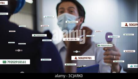 Männlicher Arzt, der ein Handgerät hält und Patientendaten im Klinikkorridor mit Datenüberlagerungen anzeigt Stockfoto