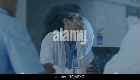Arzt in Peelings mit Stethoskop, das Tablettendaten im Besprechungsraum des Krankenhauses mit 3D-Globus überprüft Stockfoto