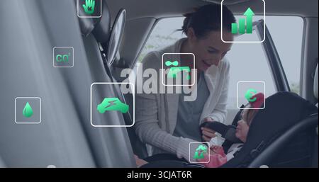 Kniende Pflegekraft, die das Gurtzeug um das Baby im hinteren Kindersitz des Autos befestigt, mit Öko-Symbolen Stockfoto