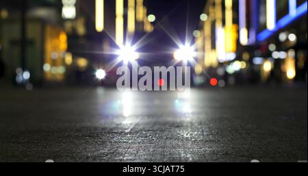 Die leuchtenden Fahrzeugscheinwerfer erzeugen auf der Nachtstraße Lichtreflexe mit reflektierendem Asphalt Stockfoto