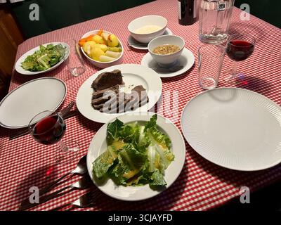 Ein silberfarbener Rumpffschnitt oder Tafelspitz auf einem Tisch für zwei Personen mit Beilagen aus grünem Salat, Kartoffeln, Gemüse, zwei Saucen, Rotwein und Wasser Stockfoto