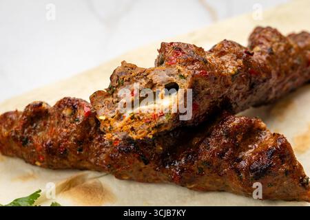 Nahaufnahme von gegrilltem Kebab mit geschmolzenem Käse auf Fladenbrot, saftig und scharf Stockfoto