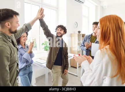 Zwei Männer geben High Five, um geschäftliche Erfolge mit jungen Leuten im Amt zu feiern Stockfoto