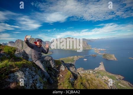 Fantastische Landschaft der Lofoten-Inseln von der Spitze des Berges Reinebringen mit blauem Himmel, Norwegen. Mann auf einem Berg, der ein Selfie in Norw macht Stockfoto