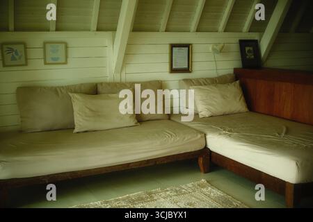 Tabanan, Bali, Indonesien – 26. August 2025: Minimalistisches L-förmiges Holzsofa mit beigefarbenen Kissen in einer gemütlichen Wohnecke Stockfoto