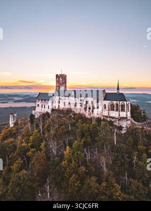 Auf einem Hügel thront Bezdez Castle mit seiner mittelalterlichen Architektur vor dem Hintergrund eines lebhaften Sonnenuntergangs im Sommer. Die alten Ruinen und der Turm bilden eine markante Silhouette am Abendhimmel. Stockfoto