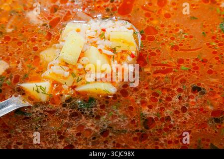 Die Oberfläche von Reissuppe mit Gemüse, mit einem vollen Löffel Suppe aufgeschöpft. Stockfoto