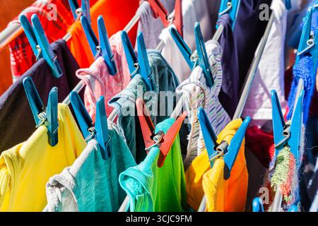 Mehrfarbige Kleidung hängt an Kleiderschalen und trocknet nach dem Waschen in Nahaufnahme. Stockfoto