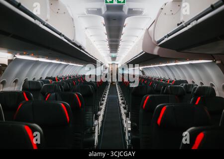 Blick auf eine leere Kabine für gewerbliche Flugzeuge mit Reihen schwarzer Sitze mit roten Akzenten. Die Dachfächer sind geschlossen, und es sind keine Passagiere anwesend Stockfoto