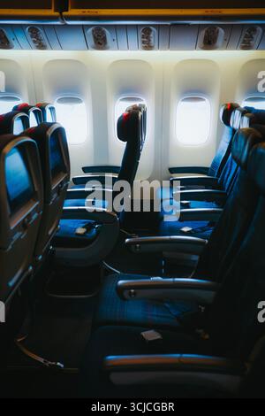 Eine leere Flugzeugkabine mit Reihen blau gepolsterter Sitze mit Sicherheitsgurten, Fensterblick und Ablagefächern über der Decke, die tr betonen Stockfoto