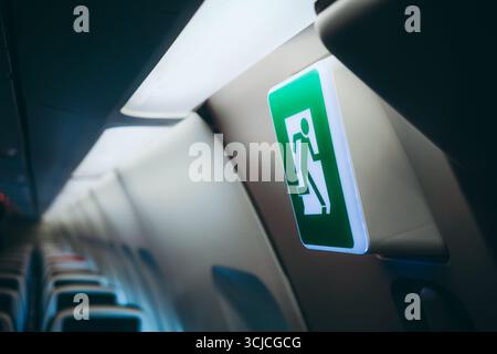 Nahaufnahme eines beleuchteten Notausstiegsschilds in einer Flugzeugkabine. Das Schild dient als Orientierung für die Passagiere, wobei Sitzreihen sichtbar sind, e Stockfoto
