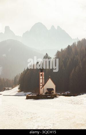 Eine ruhige Winterlandschaft in den Dolomiten, Italien, mit einer malerischen Kirche umgeben von schneebedeckten Böden und dichten Wäldern, mit majestätischen Bergen Stockfoto