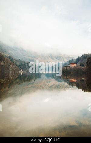 Ruhige Winterlandschaft in den Dolomiten, Italien, mit einem ruhigen See, der die umliegenden Bäume und Berge mit leichtem Nebel reflektiert Stockfoto