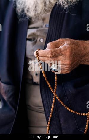 Abgeschnittene, nicht erkennbare Nahaufnahme einer älteren Hand mit einer Tasbih, die Reflexion und Hingabe symbolisiert. Die Hand des Mannes, mit einem Ring geschmückt, sanft Stockfoto