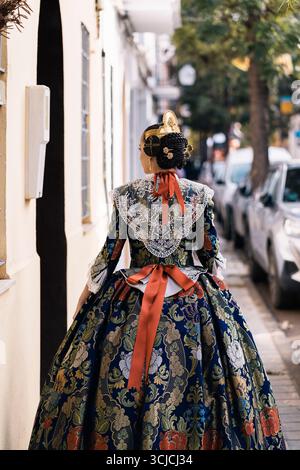 Während des Las Fallas Festivals in Spanien spaziert eine Frau in einem exquisiten Fallera-Outfit entlang einer valencianischen Straße und zeigt das reiche kulturelle Erbe A Stockfoto