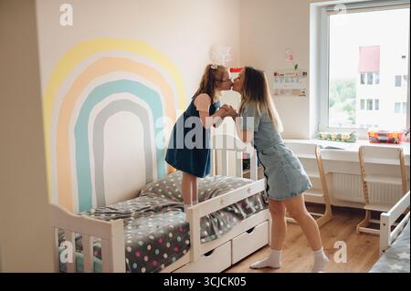 Ein berührender Moment zwischen einer Mutter und ihrer Tochter mit Down-Syndrom, während sie einen liebevollen Kuss teilen, Seite an Seite auf dem Bett stehen in einem gemütlichen, warmen Ambiente Stockfoto