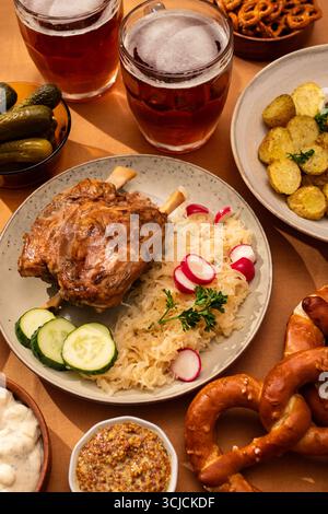 Ein herzhaftes deutsches Festmahl mit saftiger Schweinshaxe mit Sauerkraut, Radieschen und Gurken. Begleitet von Kartoffelsalat, Brezeln, Senf und Stockfoto