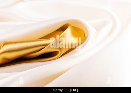 Eleganter Hintergrund aus Satin mit luxuriösen Falten in sattem Gold und weichen Elfenbeintönen. Die glatte Textur und die glänzende Qualität sorgen für Raffinesse Stockfoto