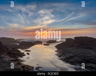 Atemberaubender Sonnenuntergang an der Küste Oregons mit leuchtenden Farben, die sich vom ruhigen Wasser reflektieren. Der Himmel ist mit Orange- und Rosa-Tönen bemalt, was einen erzeugt Stockfoto