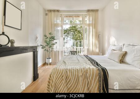 Ein helles und luftiges, modernes Schlafzimmer mit großen Fenstern und Tageslicht. Das Dekor vereint Einfachheit und Eleganz mit Erdtönen und einem Hauch Stockfoto