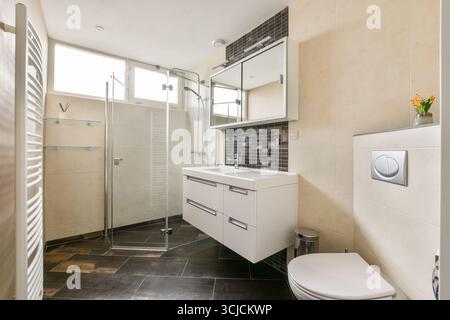 Modernes Bad mit Glasdusche, stilvollem Waschbecken und eleganten Fliesen, die Funktionalität und ästhetisches Erscheinungsbild verbessern. Stockfoto