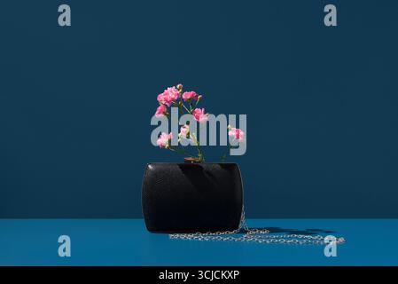 Ein minimalistisches Bild mit wunderschönen rosa Blumen, elegant in einer schicken schwarzen Tasche platziert, vor einem leuchtend blauen Hintergrund und verkörpert natürliche Schönheit Stockfoto
